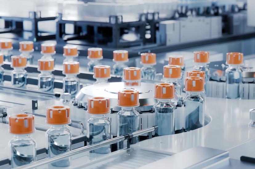 A series of clear glass drug vials with orange caps on a production line