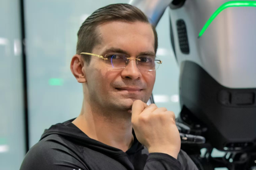 A white man with short dark hair and glasses sits with his finger rested on his chin
