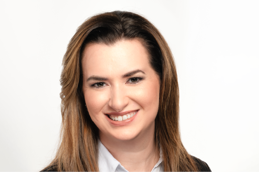 A white woman with long brown hair and brown eyes wearing a white shirt and dark pullover