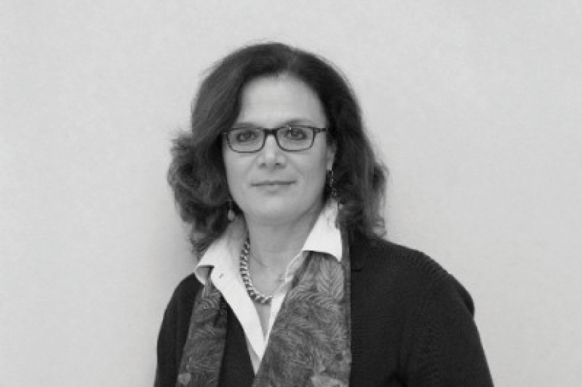 A black and white image of a white woman with long, dark hair, glasses and a scarf