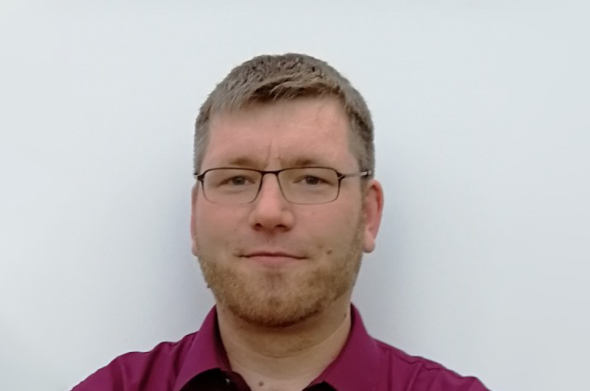 A white man with fair hair and glasses wearing a red shirt
