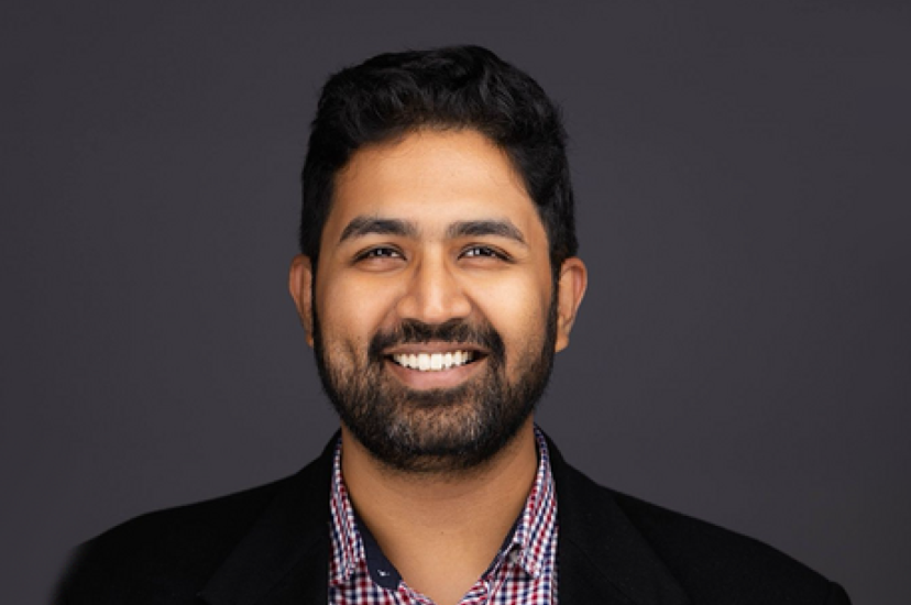 An Asian man with dark hair and beard wearing a dark jacket and ginghamshirt