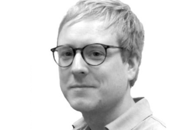 A monochrome image of a white man with short hair and glasses