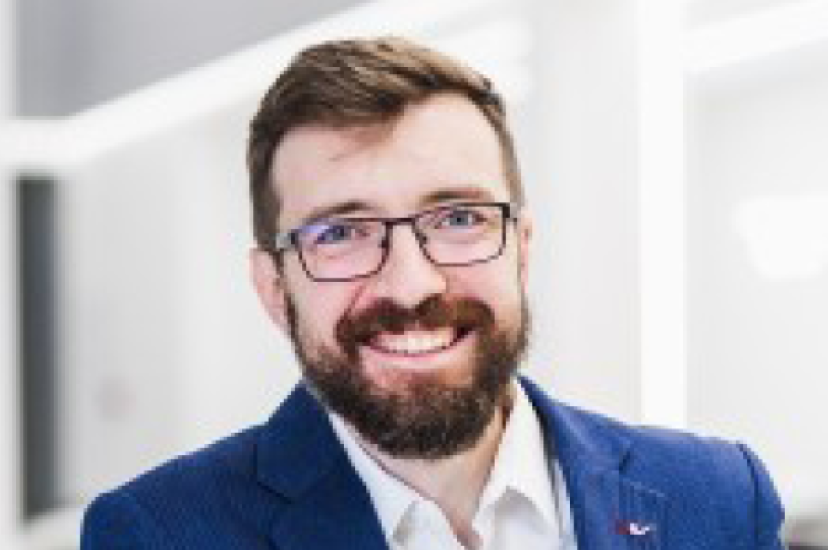 A white man with brown hair, glasses and a beard wearing a blue suit