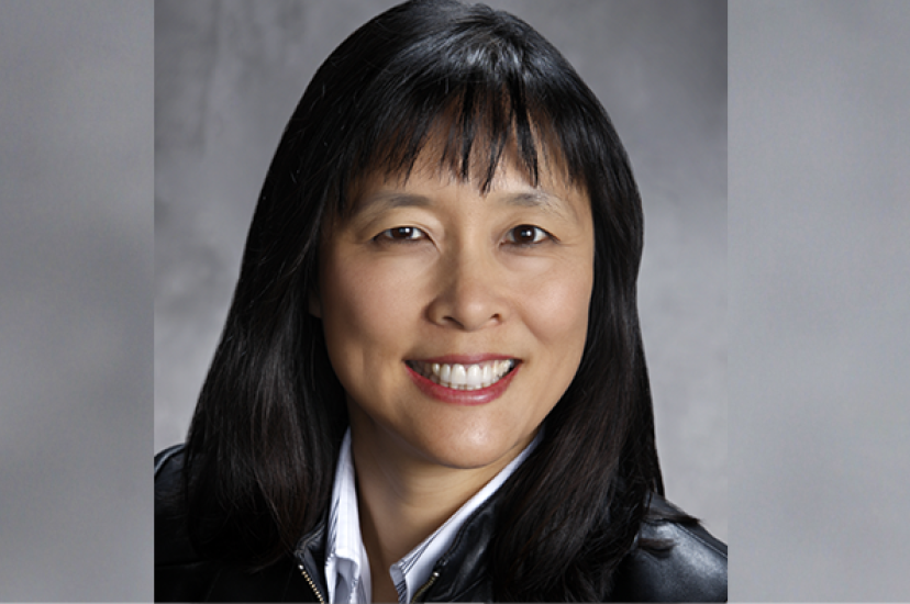 An Asian woman with black hair wearing a black leather jacket before a grey background
