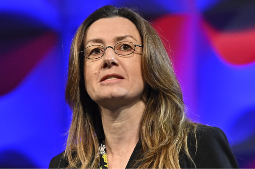 A woman with long brown hair stands before a multicoloured background