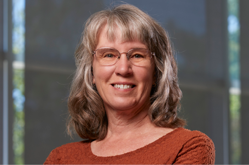 A white woman with fair hair, wearing a rust-coloured top