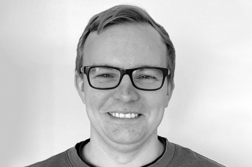 A monochrome image of a white man with short hair and glasses