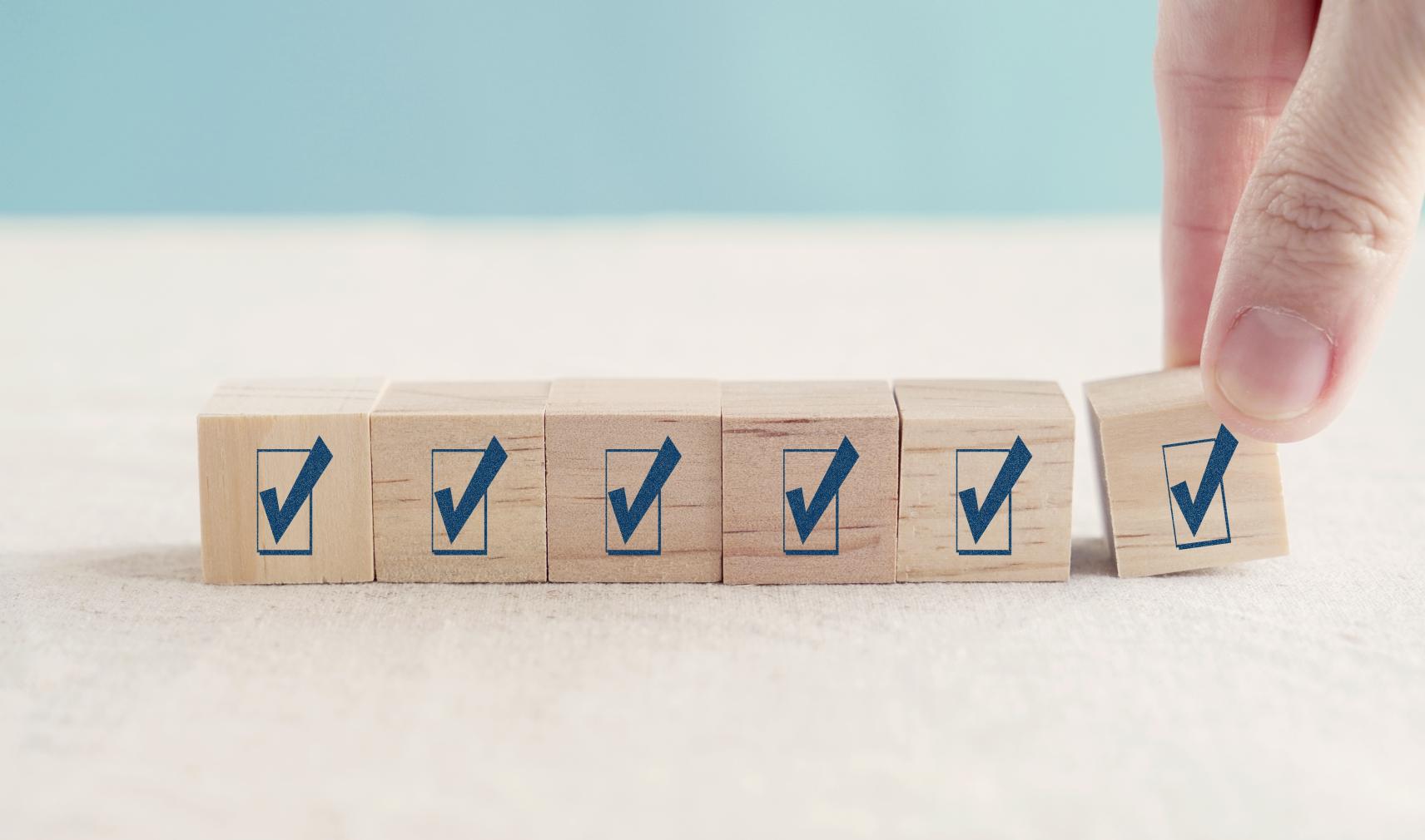 A hand placing the final check-mark block in a row of wooden cubes, representing participation in the 2026 Storage Survey on AI, HPC and data-intensive research.