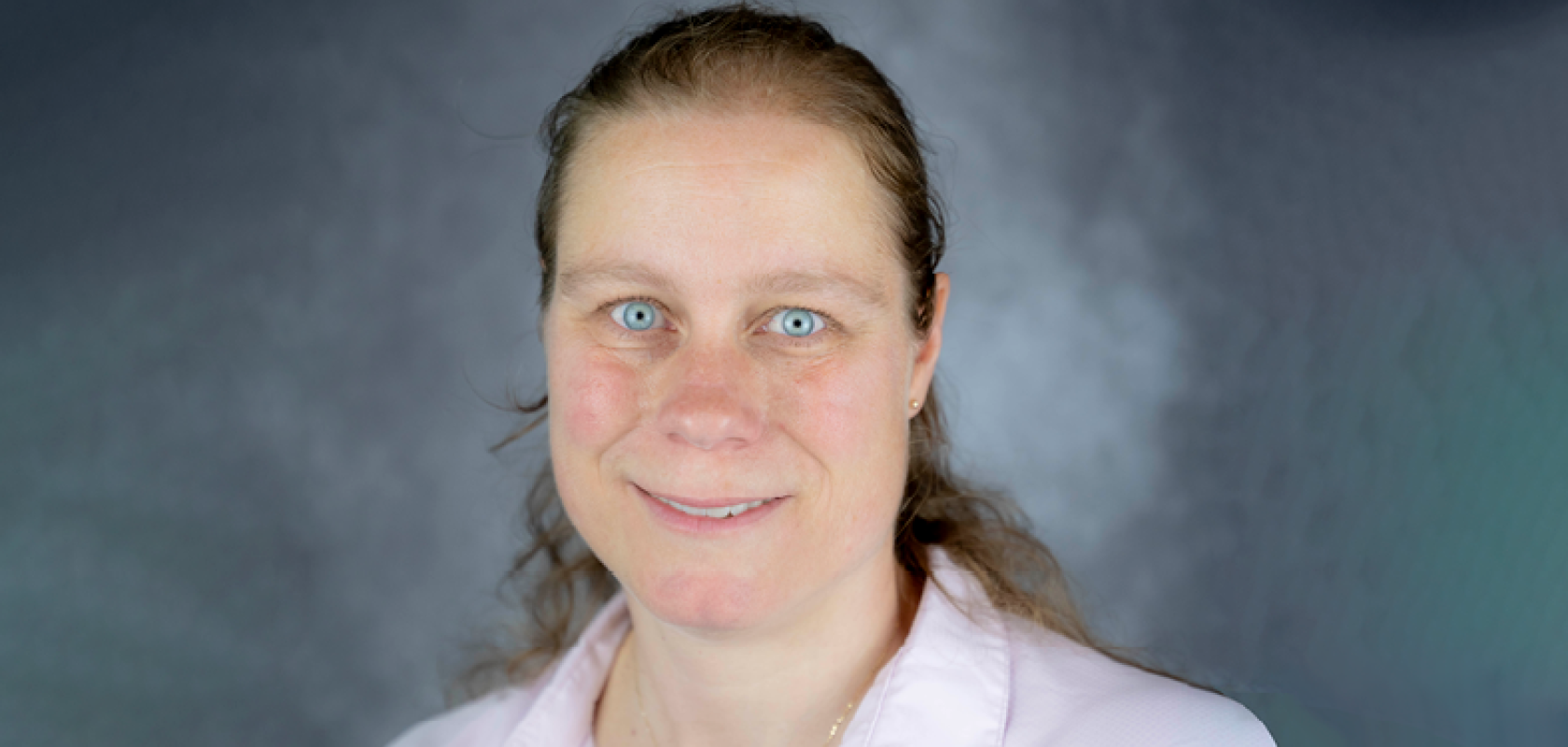 A white woman wearing a pink shirt against a green background