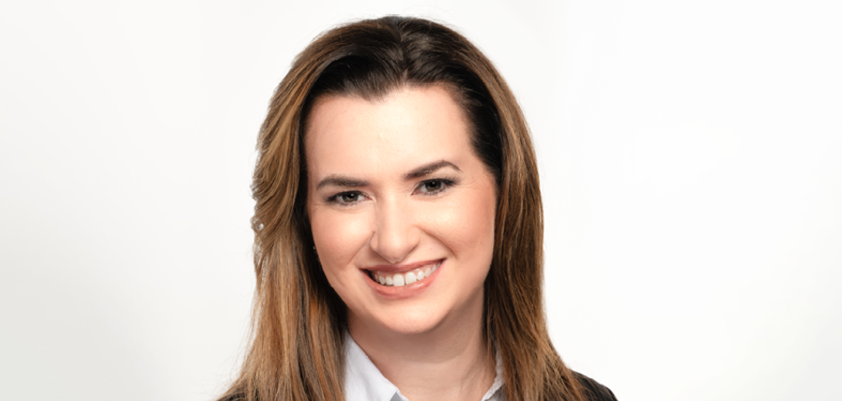 A white woman with long brown hair and brown eyes wearing a white shirt and dark pullover
