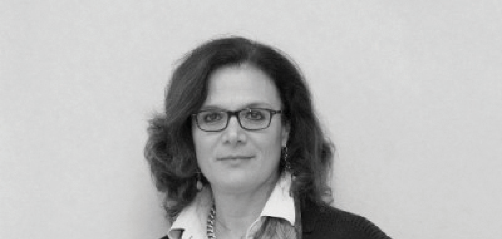 A black and white image of a white woman with long, dark hair, glasses and a scarf