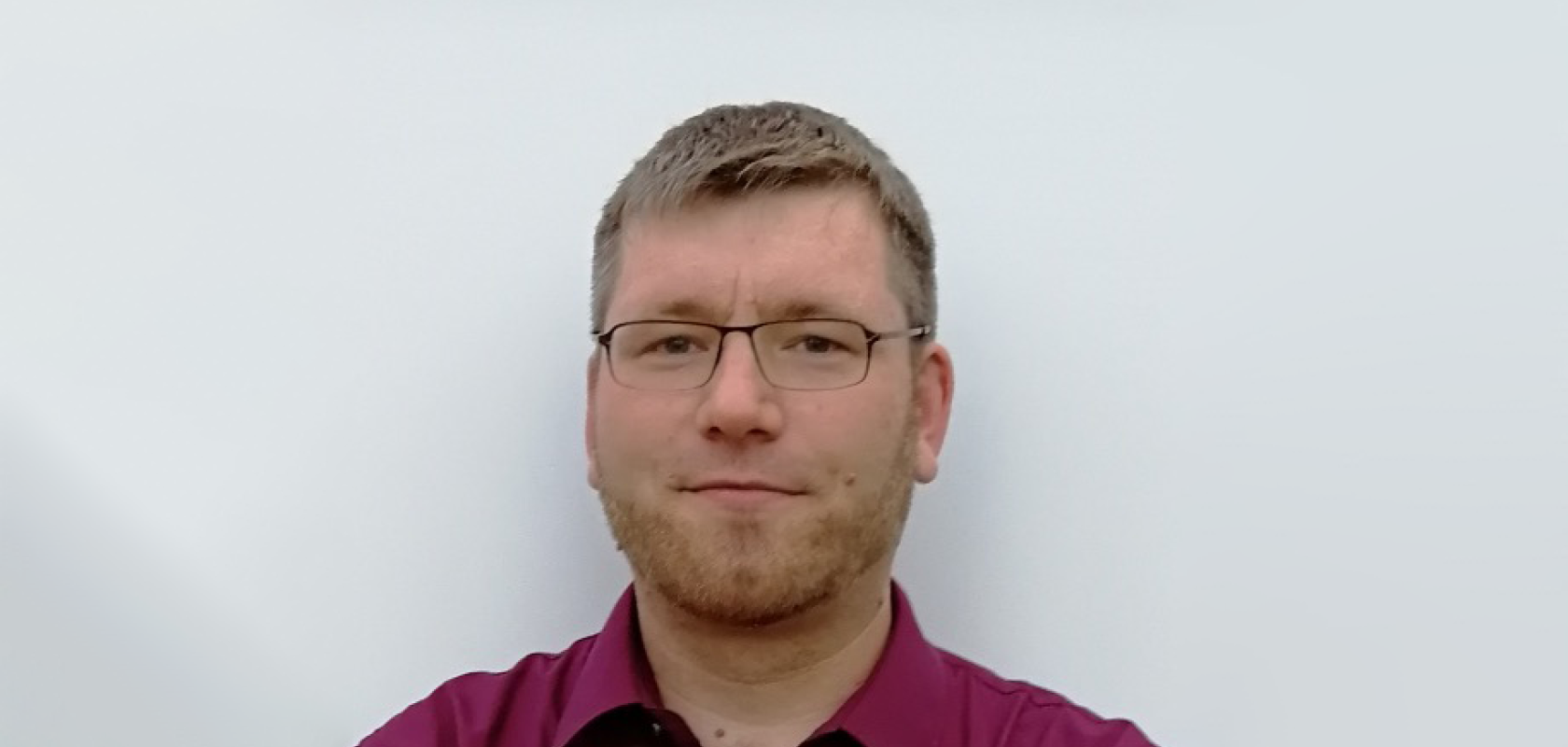 A white man with fair hair and glasses wearing a red shirt