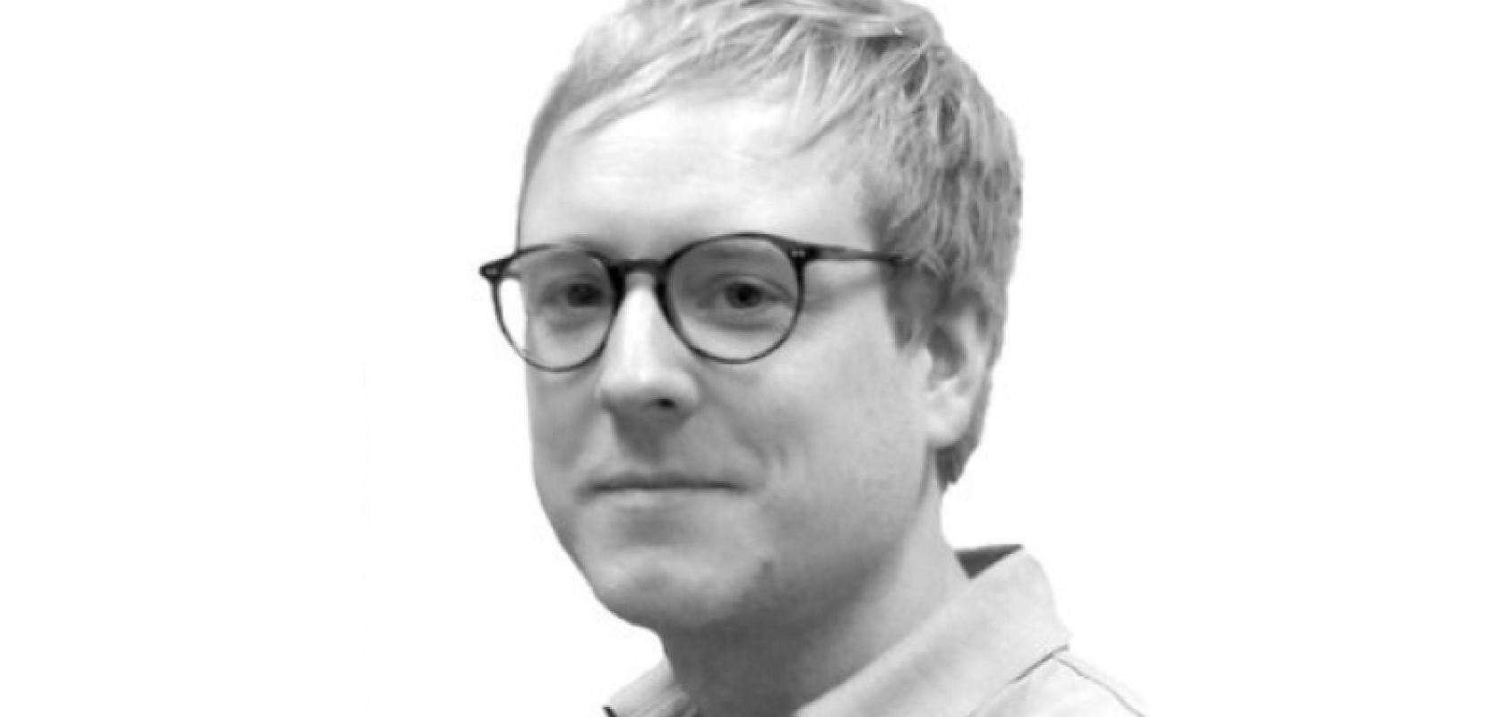 A monochrome image of a white man with short hair and glasses