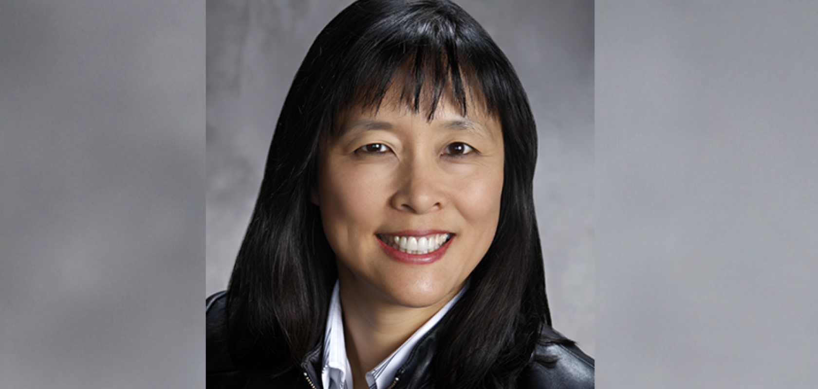 An Asian woman with black hair wearing a black leather jacket before a grey background