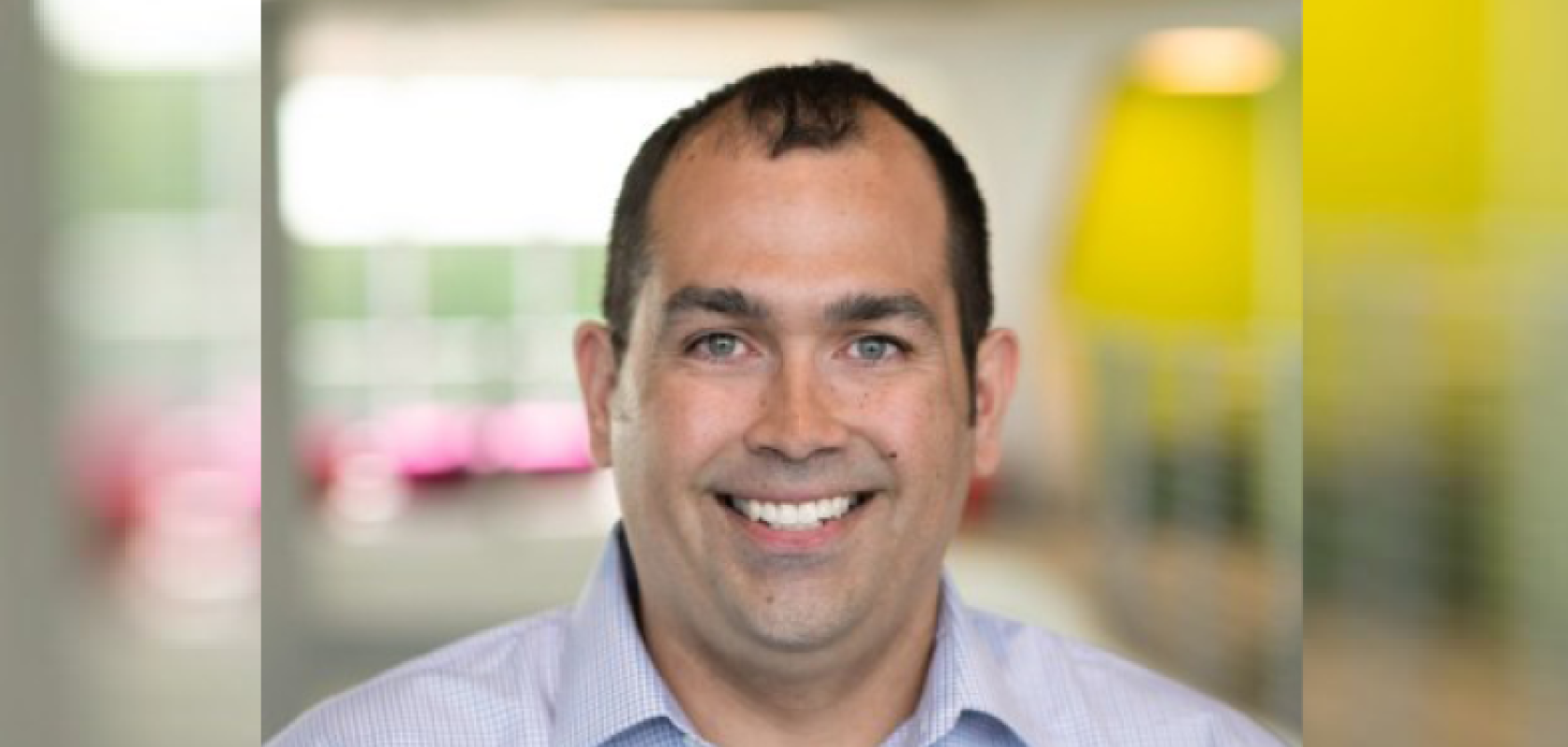 A white man smiles at the camera. He is wearing a striped shirt 