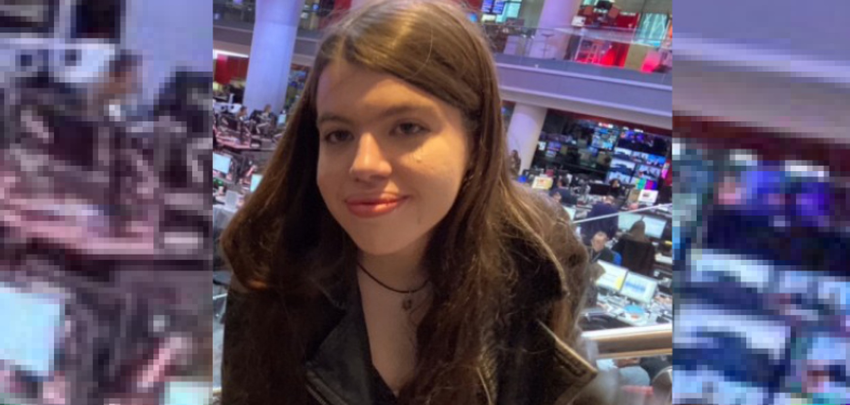 A woman with long brown hair sits with her back to a news studio
