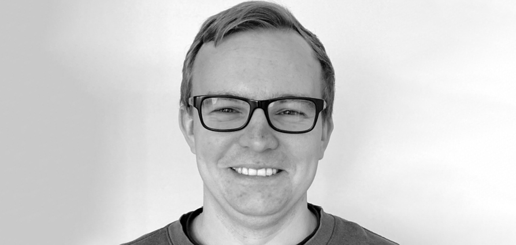 A monochrome image of a white man with short hair and glasses