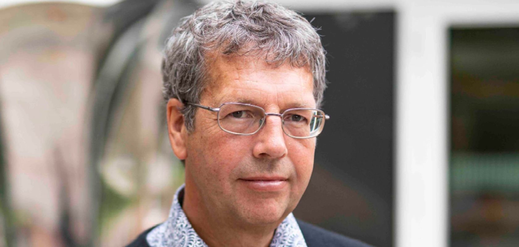 A white man with greying hair and glasses, wearing a shirt and jumper