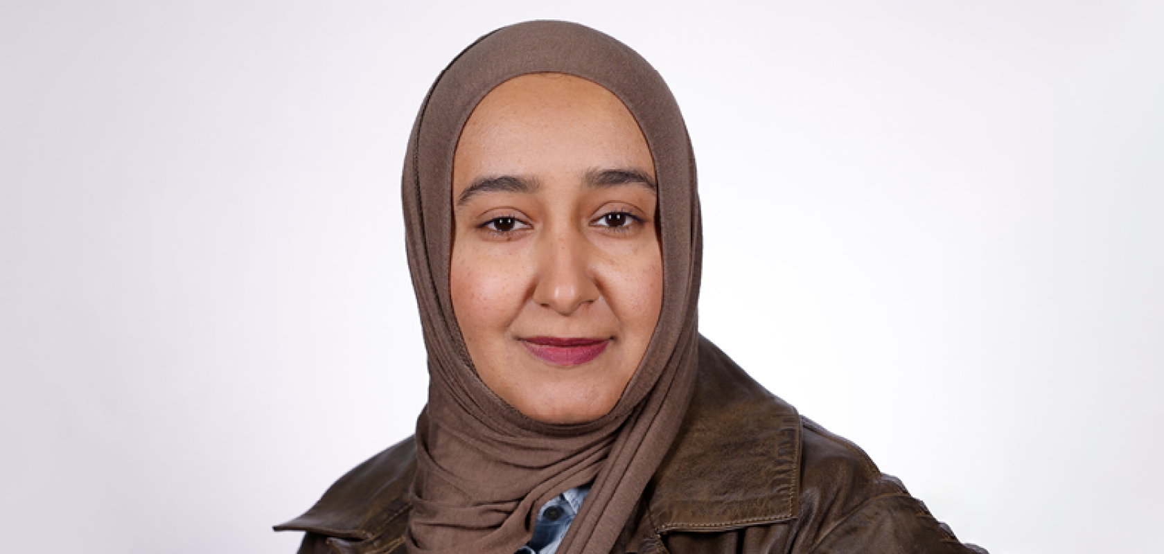 A Middle Eastern woman with brown eyes, is wearing a brown hijab and a brown leather jacket