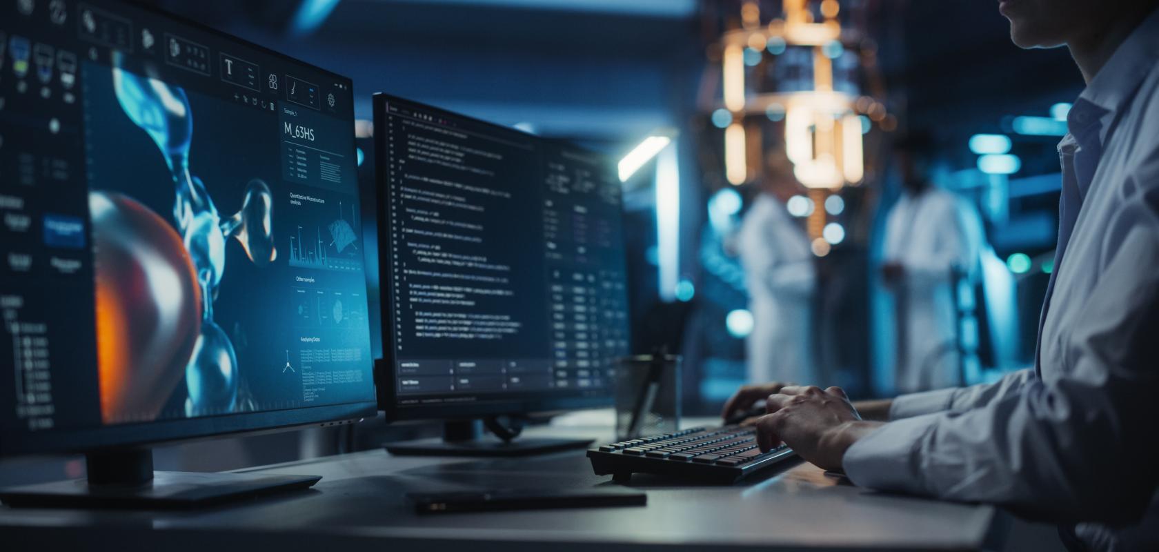 Researcher analysing scientific data across two screens while using a keyboard.